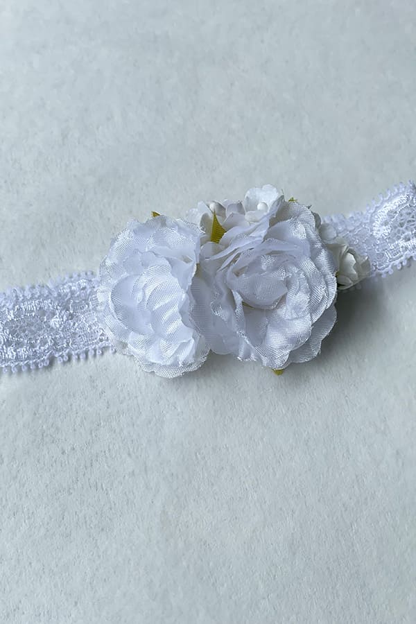 Bandeau cheveux pour bébé fille en dentelle et fleurs blanches. A porter pour un baptême ou une cérémonie. Photo du gros plan des fleurs blanches.