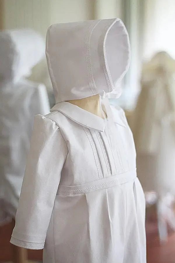 Barboteuse baptême bébé garçon Léo en coton blanc et dentelle de coton. Création française Fil de Légende. Photo de la barboteuse portée avec le bonnet de baptême assorti.