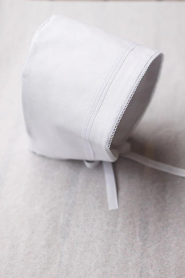 Bonnet de baptême bébé garçon Léo en coton blanc et galons de dentelle de coton. Création française Fil de Légende. Photo du bonnet vu de côté.