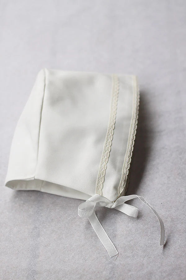 Bonnet de baptême bébé garçon Oscar en coton blanc cassé et dentelle de coton ivoire. Création française Fil de Légende. Photo du bonnet vu de côté.