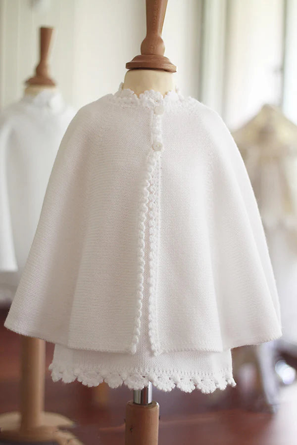 Cape de baptême en maille tricotée blanche avec une bordure festonnée faite au crochet à la main. Création française Fil de Légende. Disponible en ligne ou en boutique à Paris, Neuilly-sur-Seine.