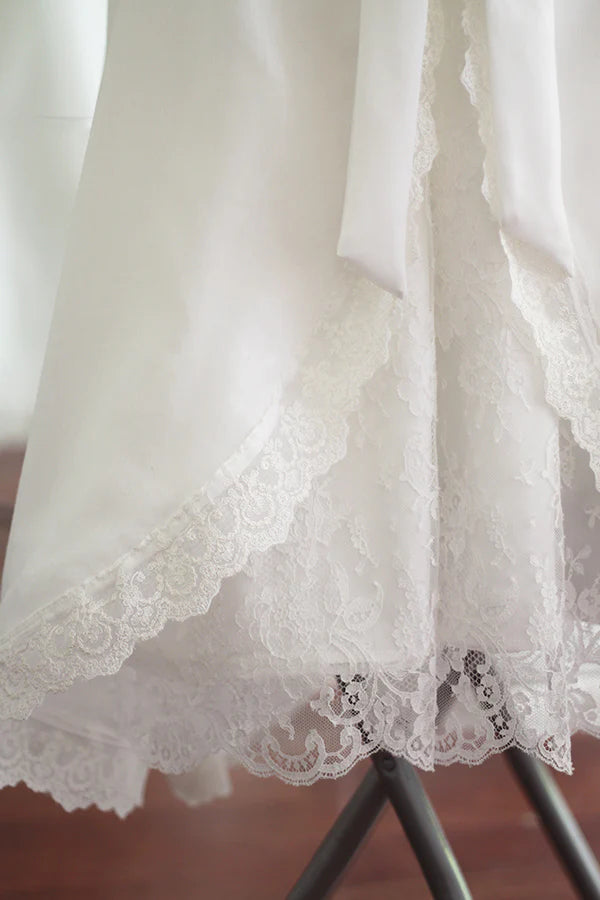 Cape de baptême longue traditionnelle pour baptême en mousseline blanc cassé et dentelle fine. Se ferme avec un large ruban. Fait main en France. Gros plan sur dentelle.