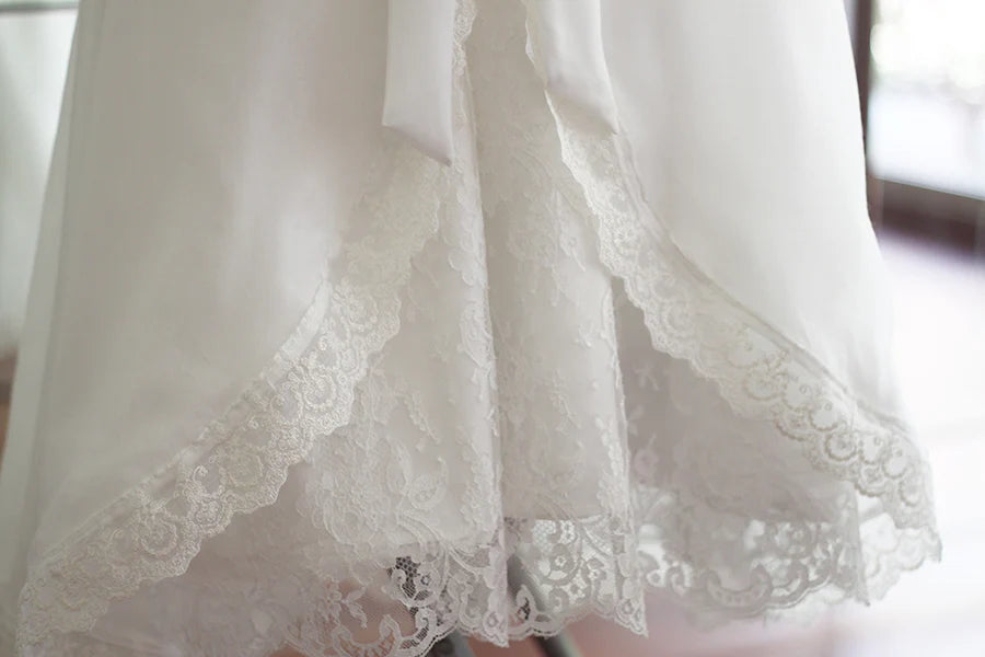 Cape de baptême longue traditionnelle pour baptême en mousseline blanc cassé et dentelle fine. Se ferme avec un large ruban. Fait main en France. Gros plan sur les dentelles.