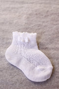 Chaussettes bébé fille en coton blanc ajourées avec un bord dentelé et un noeud en satin blanc sur le côté. A porter avec une robe de cérémonie bébé ou une robe de baptême - Fil de Légende Paris, Neuilly-sur-Seine
