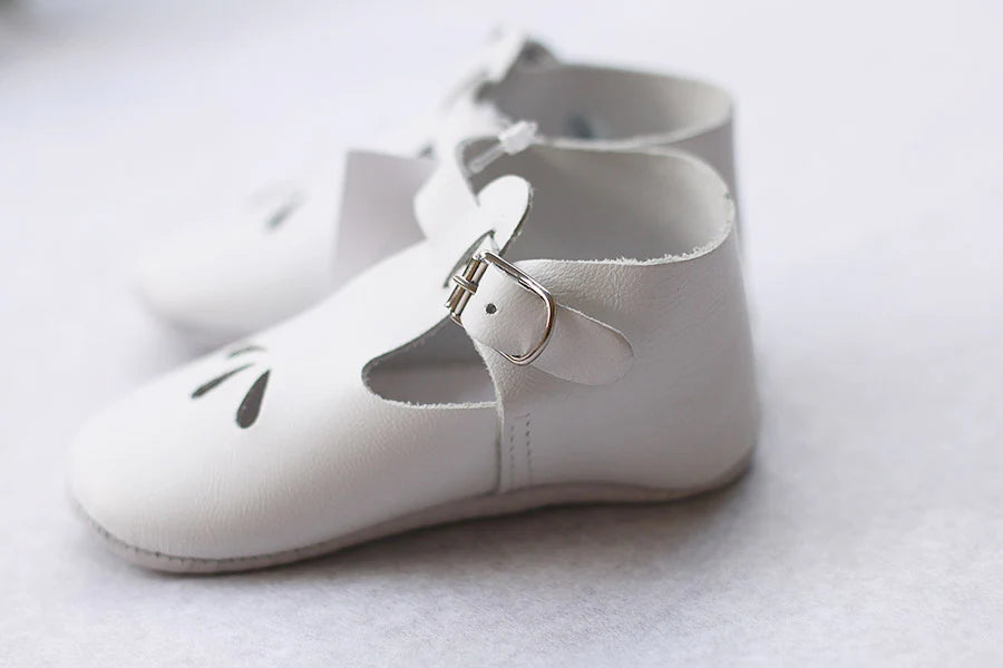 Chaussons cérémonie baptême bébé en cuir blanc. Idéal pour la saison printemps/ été. Ouverture à boucle. Gros plan sur chaussons.