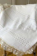Couverture bébé pour cérémonie ou baptême en lainage blanc cassé, avec motifs ajourés et large galon de dentelle. Magasin Fil de Légende Paris, Neuilly-sur-Seine.