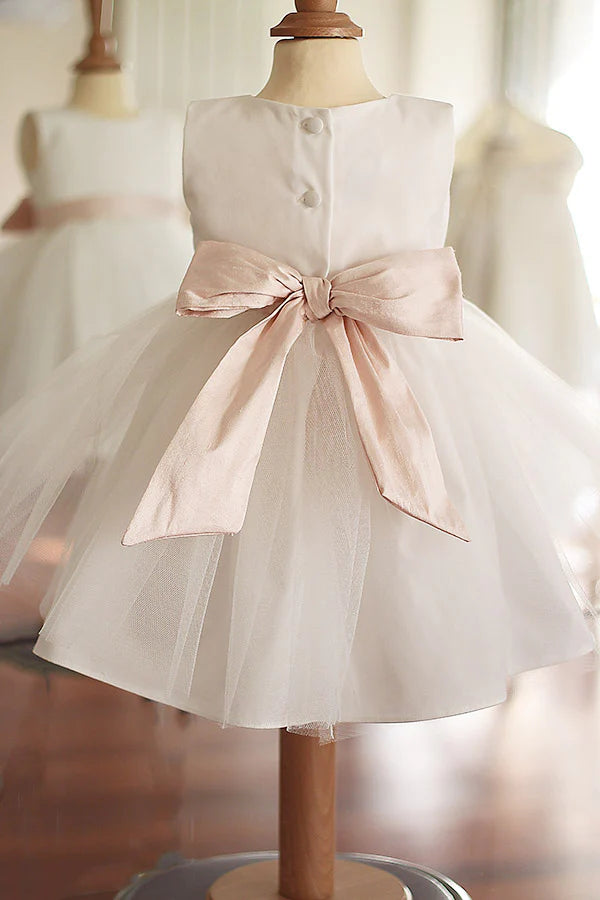 Robe de baptême ou de cérémonie pour bébé fille en coton blanc cassé avec une jupe en tulle et une ceinture rose poudré. Photo du noeud rose.