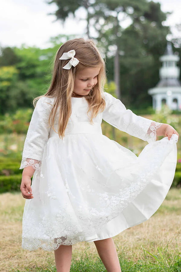 Robe de baptême et de cérémonie pour bébé et petite fille, en tulle brodé blanc cassé doublé de satin. Robe automne-hiver manches longues. Création française Fil de Légende. Photo de la robe portée par une petite fille.
