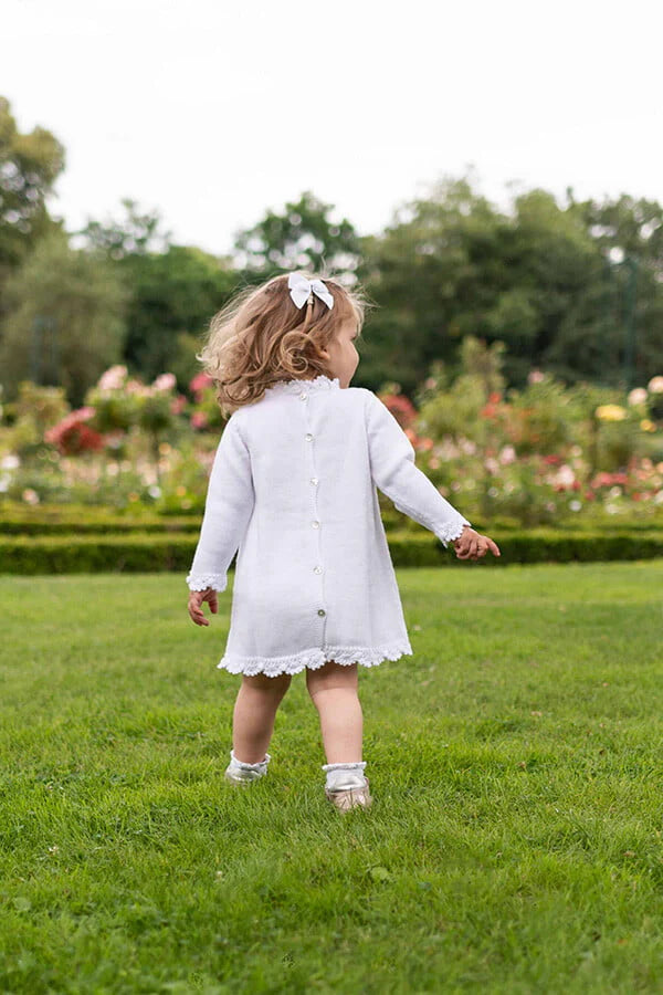 Robe baptême fille blanc cassé en maille tricotée avec bordures faites au crochet à la main. Robe en lainage. Création française Fil de Légende. Photo de la robe portée par une petite de dos.