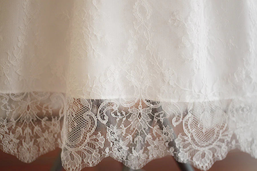 Robe de baptême traditionnelle bébé en dentelle fine de couleur blanc cassé. Corsage manches longues. Cousu main en France. Gros plan bordure dentelle.